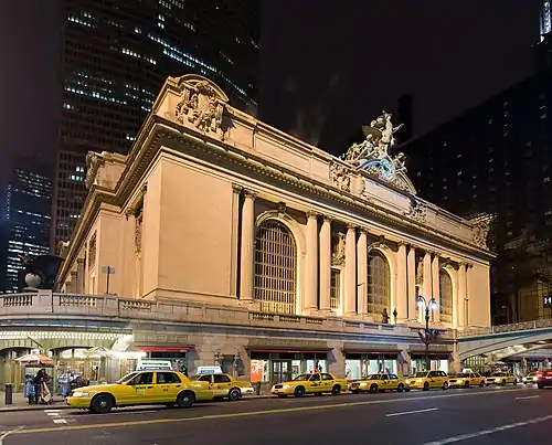 A row of yellow taxis in front of a multi-story ornate stone building with three huge arched windows.