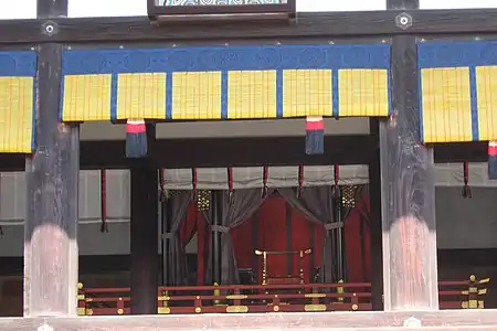 Throne on display in the Kyoto Imperial Palace; from outside inwards, blue-bound misu blinds, pillar slots for shitomi shutters (currently removed), white kabeshiro (wall-curtains) caught up with red-and-black nosuji (野筋) ties, and chōdai (canopy and dais, in red and purple). Older styles often persist in rare ceremonial use.