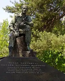 Bronze statue with light green patina depicting a seated soldier with his arm resting on his leg, gazing downward