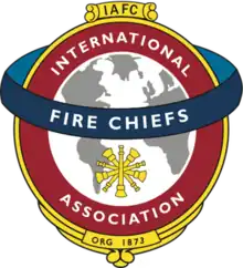 A white and gray globe surrounded by a red circle reading "International Association," with a blue band running horizontally across the circle reading "Fire Chiefs"