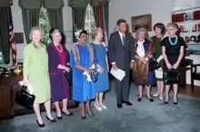 Seven women standing in a row with the President, in the Oval Office, in 1963.