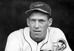 A close-up of a man wearing a baseball uniform with a cartoon oriole on the right sleeve and a realistic oriole on the cap.