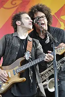 Clemons and Lofgren singing into the same microphone as Lofgren plays guitar