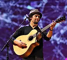 A Caucasian man wearing a bucket hat strums a guitar