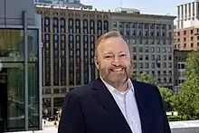 Jay M. Bernhardt in blue blazer with Little Building, Colonial Building behind him.