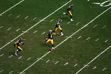 Four players run up the field as the kicker executes a kickoff