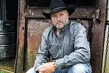 Country music singer Jeff Carson, kneeling in front of a rusty door