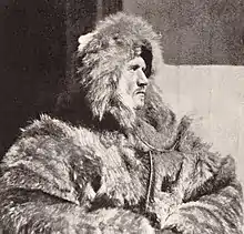 Head and upper body of a man, facing right. He is dressed in heavy fur clothing including a hat which conceals much of his face, although the profile is clear