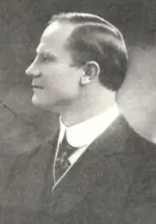 A white man in profile, wearing a dark suit and tie