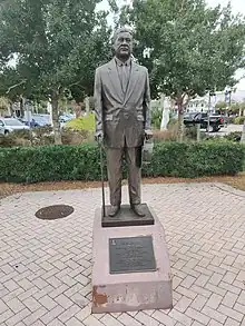 Statue of elderly man in suit, holding a brimmed hat and walking stick.