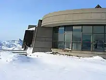 Surrounding a curved building with glass windows is a landscape of snow.