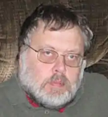 Middle-aged man wearing eyeglasses, a gray sweater, with black and gray hair, and a gray-haired beard