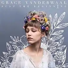 Head and shoulders of Grace VanderWaal, a teenage girl, gazing to her right. She has flowers in her hair, which are piled on her head.