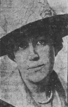 A white woman wearing a wide-brimmed hat and a strand of pearls