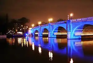 Picture of a road bridge across the river at night, illuminated with blue lights.