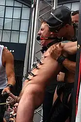 A gagged man's penis and scrotum are pulled using a rope at Folsom Street Fair. The force applied to pull should always be increased gradually.