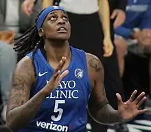 Waist high portrait of young woman wearing navy blue basketball uniform and headband with outstretched hands