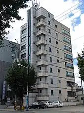 In front of a beige nine-story building, three cars parked