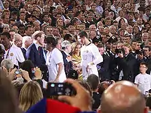 A man in a white shirt receives a medal from a man in a suit.