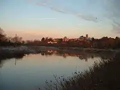 A town with church tower seen on the far side of a wide river.