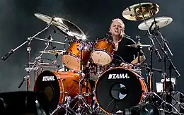 Short-haired man in a black shirt on a drum kit