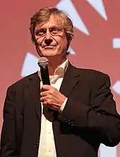 Lasse Hallström holding a mic in his left hand and looking away from the camera