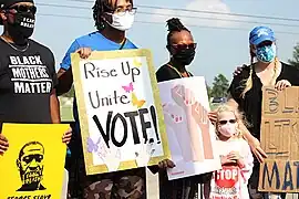 Protesters along funeral procession wearing COVID mass and holding signs