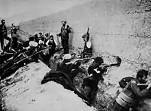 Men with guns crouching in a trench and leaning against a defensive wall