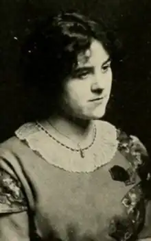 A young white woman with curly dark hair, wearing a dress with a round lace-trimmed collar