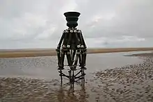 A bell in a complex wooden framework, on the beach at the edge of the sea