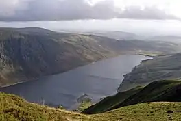 A view from a hill, looking down on a narrow lake in a valley