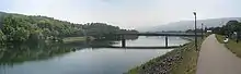 A large, smooth river crossed by a modern bridge. The left bank is tree lined, the right is a levee, a long mountain ridge is in the background.