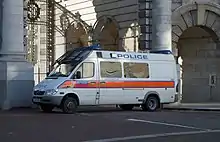 Large white van with red horizontal stripe along the midline and Police lettering near roof