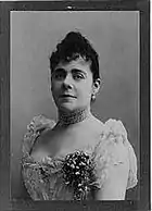 Black and white photo of a woman in a formal late 1800s dress.