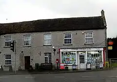 Small shop with white surrounds to the windows set in the right hand building of a terrace.