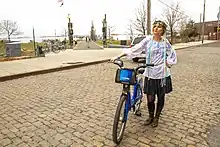 Katya Soldak standing on a road with a bicycle bearing the logo Citi-Bike