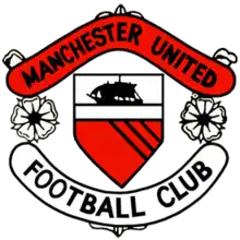 A football crest. In the centre is a shield with a ship in full sail above a red field with three diagonal black lines. On either side of the shield are two stylised roses, separating two scrolls. The upper scroll is red and reads "Manchester United" in black type, while the lower scroll is white with "Football Club" also written in black