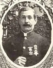 Circular portrait of a white man with a mustache wearing a military jacket with two medals pinned to the chest.