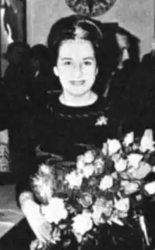 A smiling fair-skinned woman with dark hair in an updo, wearing a dark dress and holding a large bouquet