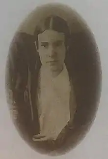 Portrait of the head and shoulders of a woman with her hair parted in the middle wearing a white blouse and dark over-blouse.