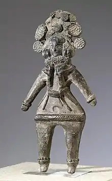 Evidence of stitching, Mathura, 3rd century BCE. A terracotta votive figurine from Mathura. The wide hips and fantastic floral headdress suggest a devotion towards fertility and abundance. She has lotus stalks in her head, and children clinging to her. Height: 25.7 cm (10.1 ″). Mathura, 3rd-2nd century BCE.