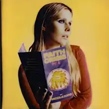 Middle Kids frontwoman Hannah Joy holding a pamphlet with the album title on it, looking upwards to her left, in front of a yellow background.