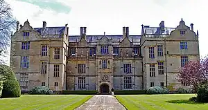 Facade of house built of yellow stone. Three floors with many large, mullioned windows and Dutch gables to the roof.