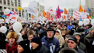 A crowd of enthusiastic protesters on Academician Sakharov Avenue, Moscow. Many balloons, posters, and flags. The protesters are bundled up on a cold overcast Winter day.