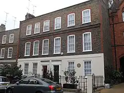 Two Georgian terraced houses in brown brick with the bottom storey in stucco, that on the right with a brown circular plaque marking Mozart's residence