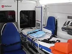 Interior view of a NKTW: transport chair (left) gurney (middle) paramedic's chair(right). One can also see the O2 - bottles (cabinet in the rear) and the medical ventilator (right foreground).