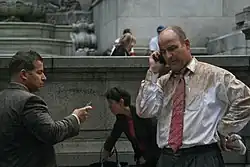 A crowd, covered in debris from the explosion. There is a businessman talking on his cellphone on the right; he has brown stains on his white shirt.