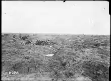 a black and white image of barren land. In the mid-ground is two field artillery guns, with teams of men at each gun, firing from left to right.