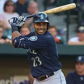 A man wearing a navy blue baseball jersey and batting helmet stands with his bat held back, awaiting a pitch.