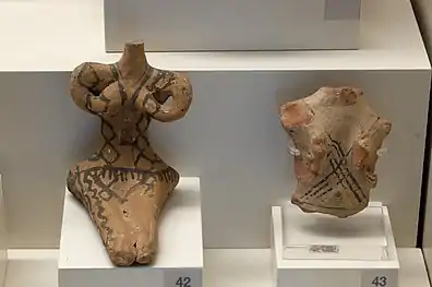 Two clay or stone figurines in a museum, apparently representing women